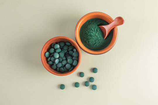 Spirulina tablets and powder in clay bowls on neutral background