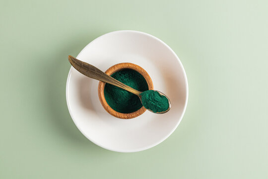 Top view of spirulina powder in bowl and spoon on plate