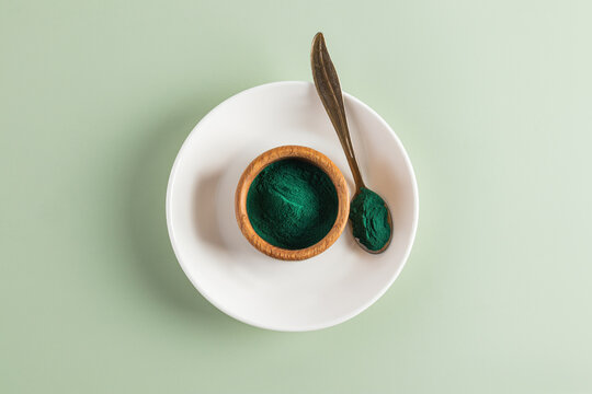 Spirulina powder in bowl and spoon on white plate