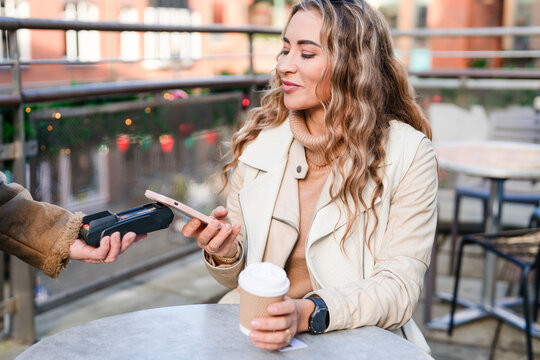 Woman enjoying coffee while making a mobile payment at a lively cafe in the afternoon