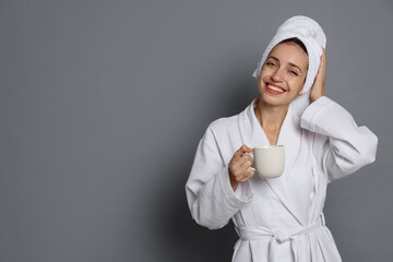 Woman in bathrobe with cup of coffee on grey background. Space for text