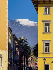 Mountain peak covered in snow seen between the buildings of a street, Riva del Garda, Italy