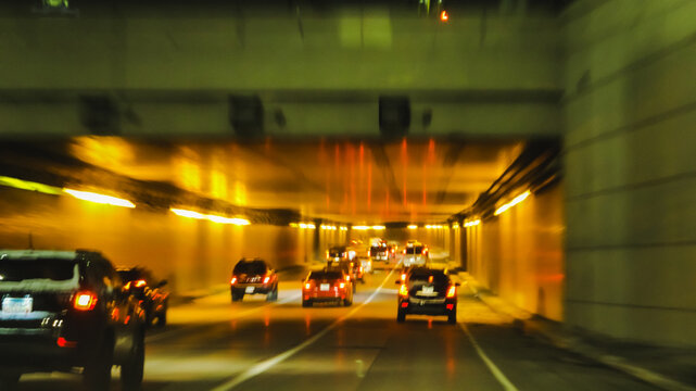 Cars in a highway tunnel under a bridge at night, captured with motion blur and warm yellow lighting. Transportation, commuting lifestyles, travel or infrastructure design element. - Powered by Adobe