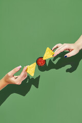 Two female hands reaching towards each other with nacho chips over salsa sauce bowl