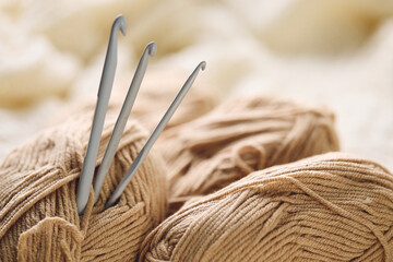 Crochet hooks and balls of beige and brown yarn on white knitted background. Knitting, crocheting supplies.