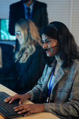 Indian customer service representative with headset typing on a keyboard while providing professional support late at night. Call center, IT support, telemarketing, online communication