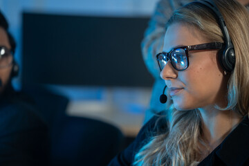 Focused female customer support agent wearing glasses and a headset, working late in a dark modern office. Technical assistance, call center, digital communication. First-Call Resolution FCR metrics