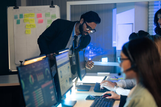 Manager, reviews data and reports on a computer screen, overseeing a diverse team in a high-pressure at command center or control room. executive is providing critical guidance on an urgent late night
