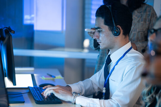 Customer service representative wearing a headset typing on a computer keyboard in modern call center office. Tech support or customer care in an efficient for business, IT, and communication