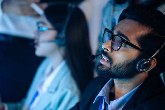 Indian man with team in a headset working call center in a control room. Customer support, IT helpdesk service, and professional telephone operations, telemarketing, sales agent at late night office - Powered by Adobe