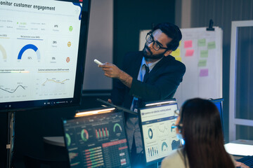 Executive is presenting customer engagement and NPS data on a large monitor in a dark office meeting. Business intelligence, corporate management, data analysis, project planning, and strategy session