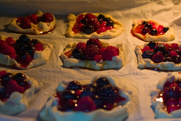 Close-up of warm berry tartlets filled with raspberries, cranberries and blueberries. Soft light highlights glossy crust and juicy berries, creating a cozy, inviting baking mood.