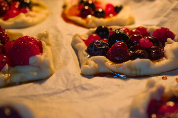 Close-up of warm berry tartlets filled with raspberries, cranberries and blueberries. Soft light highlights glossy crust and juicy berries, creating a cozy, inviting baking mood.
