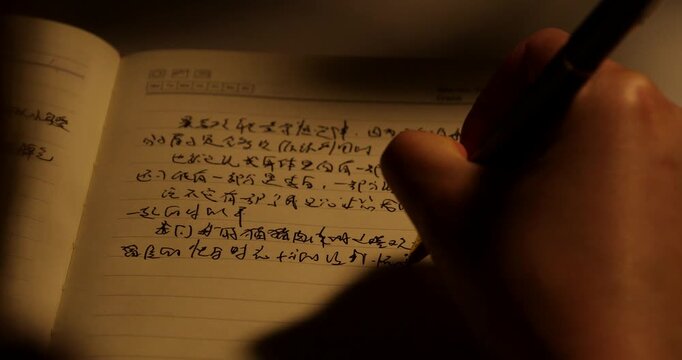 Late night study session with student writing homework in notebook under desk lamp with flowers and coffee