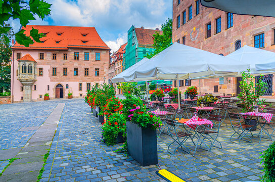 Street restaurant outdoor cafe with tables and chairs in empty square Sebalder Platz in summer day, medieval buildings in Old town Nuremberg city historical center, Middle Franconia region, Germany