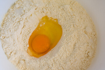 Top-view close-up of a raw egg in a flour well, capturing warm tones and detailed textures. Perfect for baking, cooking, and culinary concepts.
