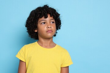 Portrait of sad little boy on light blue background, space for text