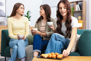 Friends with cups of drinks and treats on sofa at home