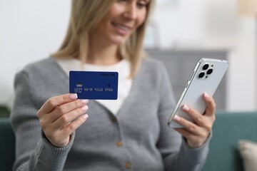 Woman making online payment with phone and credit card indoors, selective focus