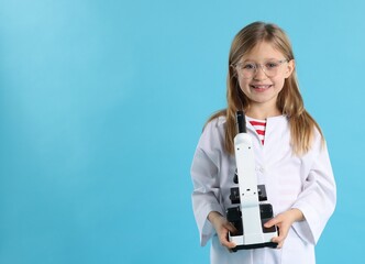 Smiling little girl in laboratory coat and glasses with microscope on light blue background, space for text. Child and science
