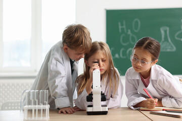 Group of children with microscope studying at desk in class. Little scientists