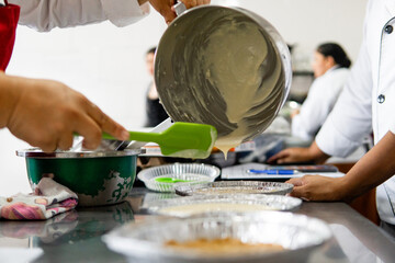 Hands pouring batter into molds during cooking class