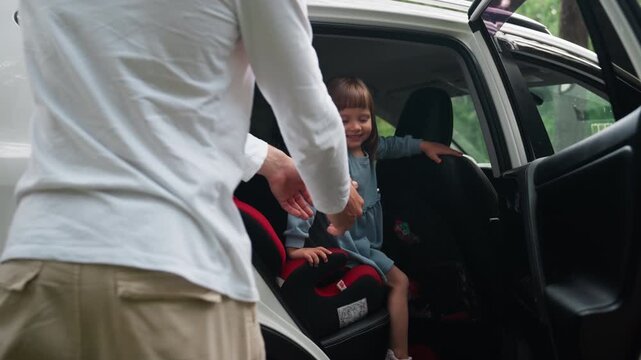 lower view shows girl opening rear door while older brother reaches in to carry excited baby sister from car seat, family suv parked among green forest, smiles, caring teamwork captured candidly
