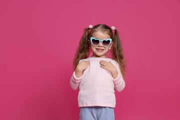 Smiling little girl in sunglasses on pink background