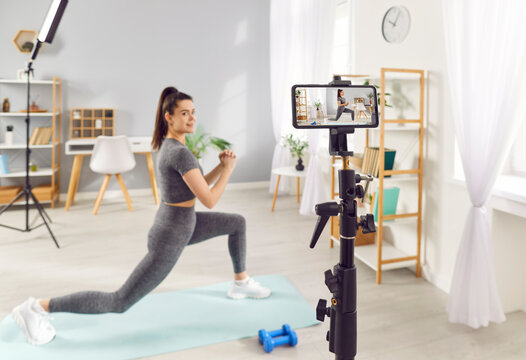 Happy woman recording herself while working out at home. Sports instructor online content creator influencer doing forward lunges filming video blog and web fitness routine workout course class lesson