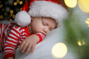 Baby in Christmas pajamas and Santa hat sleeping on bed indoors