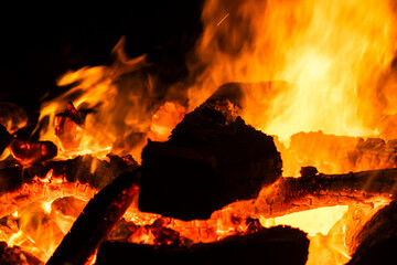 Narrow focus of a crackling bonfire at night in Brazil. Orange flames dance among stacked wood,...
