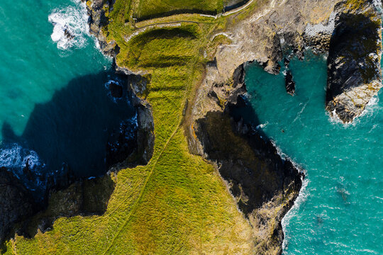 Aerial view of rugged cliffs meet the turquoise sea at St. Davids Head, where the green landscape contrasts with the dark depths below, St. Davids, Wales, United Kingdom.