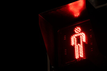 Red pedestrian traffic light signal indicating "don't walk" at night. A universal symbol of stopping, safety, warning, and waiting on a dark city street.