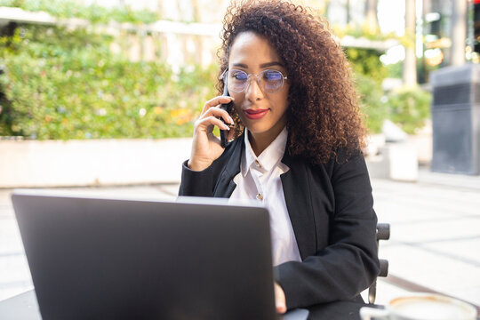 Businesswoman with curly hair using a laptop and phone