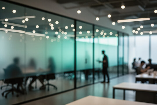 A blurred photo of a modern office interior with glass-walled meeting rooms, people in silhouette, and overhead lighting.