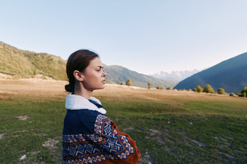 Naklejka premium Woman portrait in mountains and meadow, outdoors nature scene with thoughtful expression, standing in a landscape field wearing a patterned sweater, serene travel solitude mood.