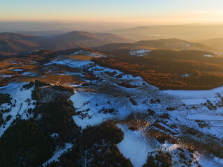 Aerial view of a snow-dusted landscape with contrasting dark forests and golden sunlit fields creating a captivating winter panorama, Detvianska Huta, Banska Bystrica Region, Slovakia.
