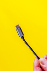 A hand holds a USB-C charging cable against a vibrant yellow backdrop, perfect for tech-related visuals