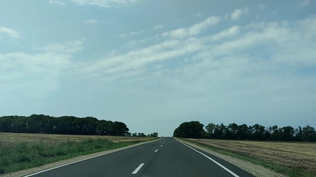 A road through fields. Driving forward along the road. A two-lane asphalt highway runs between farm fields where the harvest has already been gathered. The fields are separated by forest plantations.