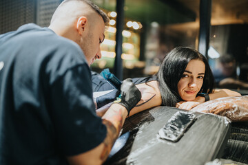 A tattoo artist wears gloves and works on a womans arm in a modern studio, ink flowing as the client relaxes and smiles. The moment captures creativity, body art, and the tattoo process.