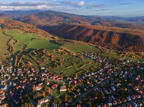 Aerial view of a charming village nestled amidst rolling hills painted with autumn's fiery hues, a tapestry of greens and golds under a vast sky, Hrochot, Banska Bystrica Region, Slovakia.