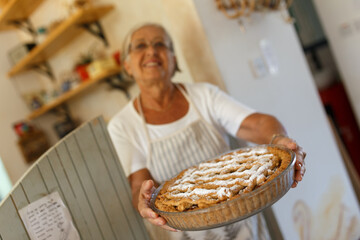 Smiling senior woman offering homemade baked apple pie