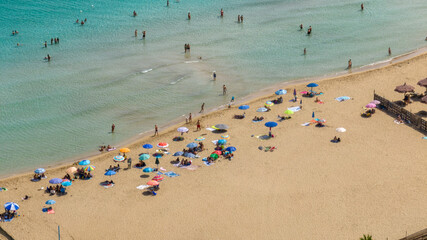 Aerial view of people on vacation with their umbrellas on a public sandy beach in Italy. This tourist destination is located in San Lorenzo, in province of Syracuse, Sicily. Summer holidays concept.