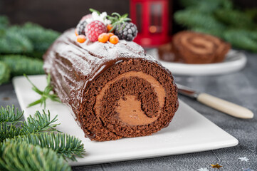 Buche de Noel. Traditional Christmas chocolate cake roll with chocolate cream, berries and glaze on a white plate. Copy space.