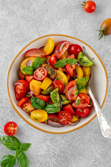 A salad of farm-fresh multi-colored tomatoes, red onions and fresh basil in a bowl on a gray concrete background. Healthy food. Top view.