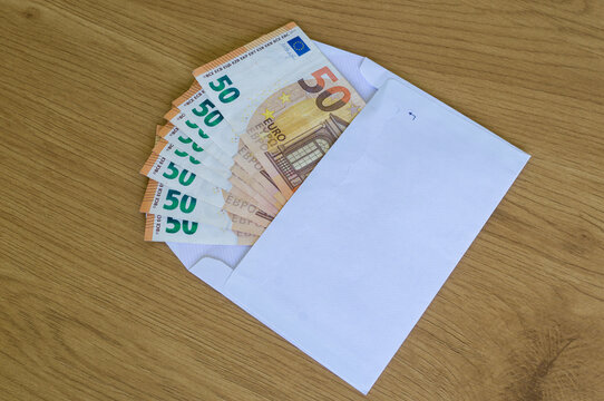 Multiple fifty Euro bills fanned out on top of an open brown paper envelope, envelope money transfer.