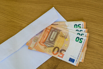 Paper money Euros in an open white envelope on a natural wood surface, budget and finance theme.