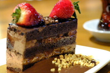 A close-up of a slice of fresh cake topped with strawberries. Tea next to a chocolate cake....