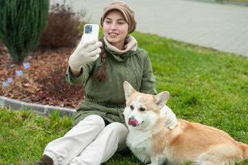 Woman walks with her dog welsh corgi in park. Stylish lady enjoys playtime whith her pet. Takes a photo of her dog.  Fall time.