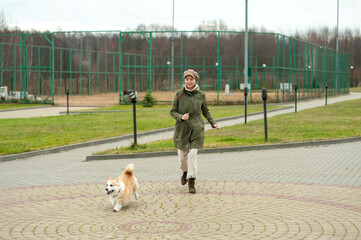 Woman walks with her dog welsh corgi in park. Stylish lady enjoys playtime whith her pet. Autumn season. Fall time.